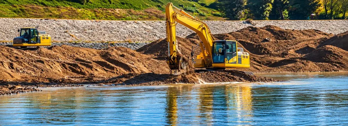 Excavator dredging sediment beside a river